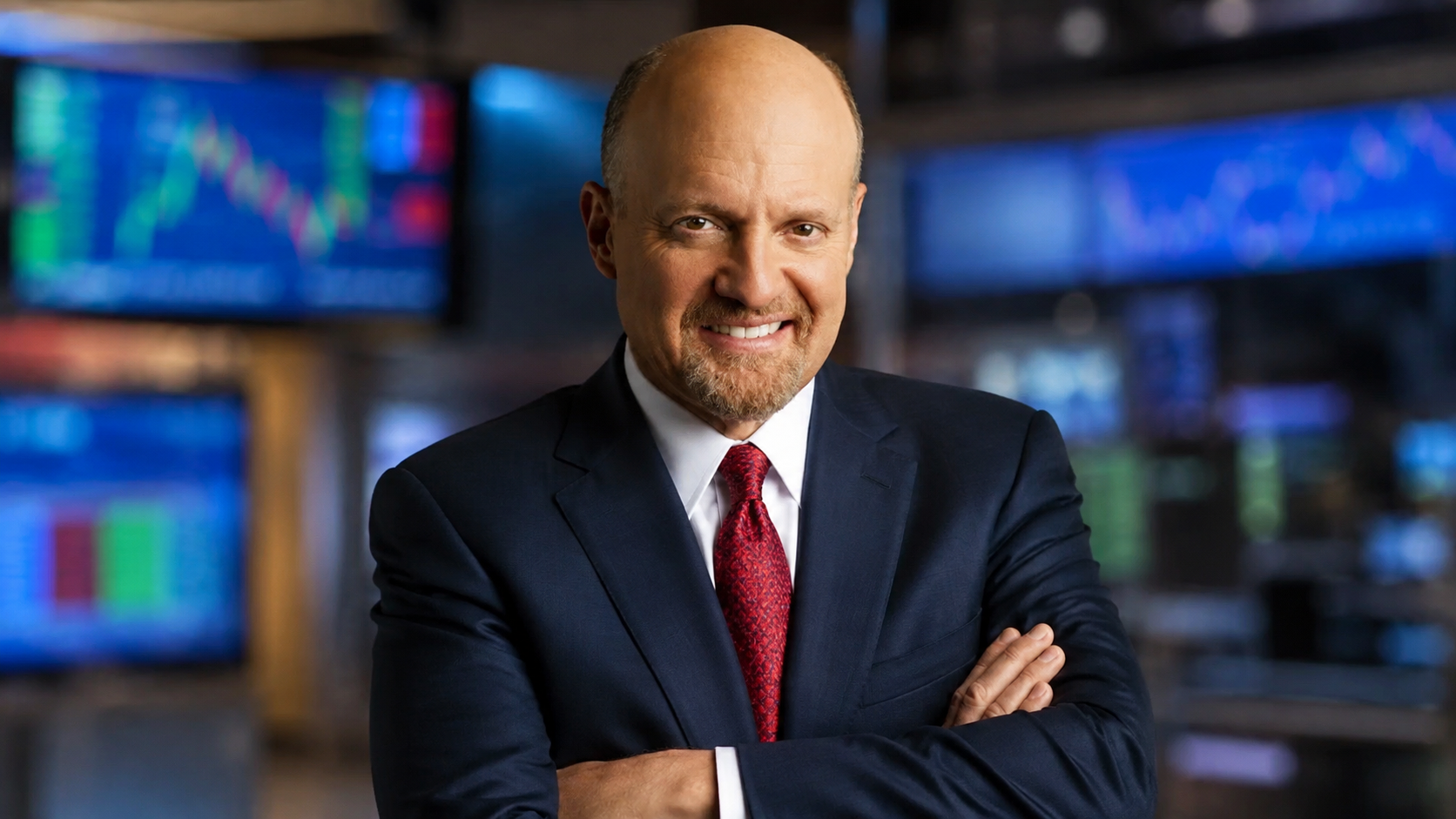 Jim Cramer in a dark suit posing against a blurred financial market studio backdrop