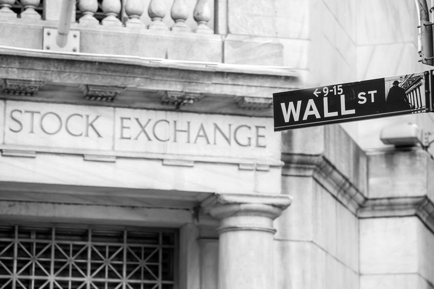 A Wall Street sign appears outside the New York Stock Exchange in a black-and-white view of Manhattan’s financial district.