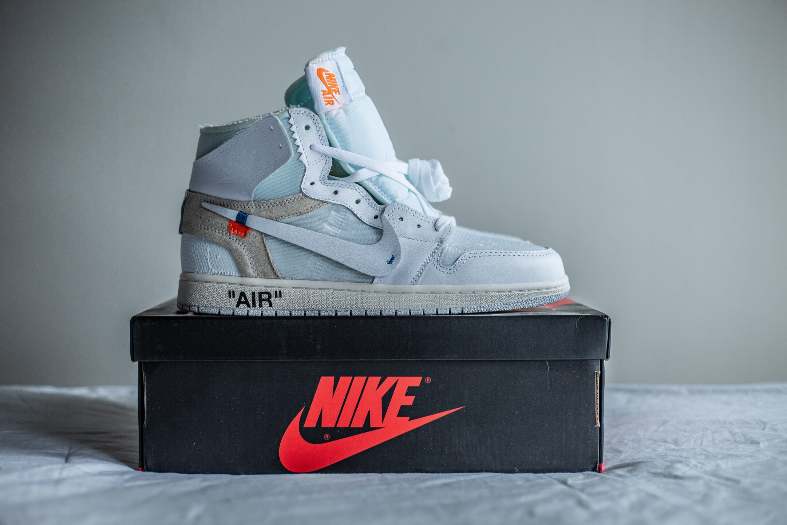 White Nike high-top sneaker rests on a black Nike shoebox, with the red Swoosh logo prominently displayed on the front.